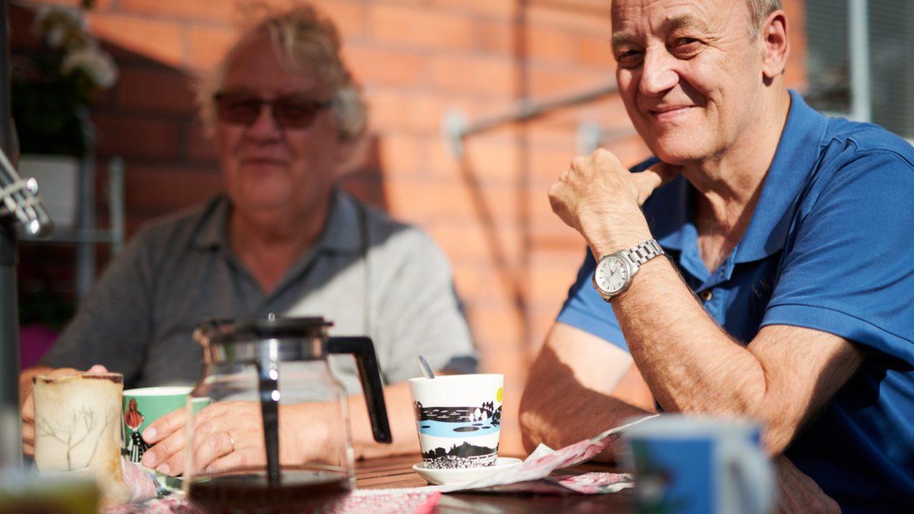 Kaksi vanhempaa ihmistä hymyilee takapihan terassilla