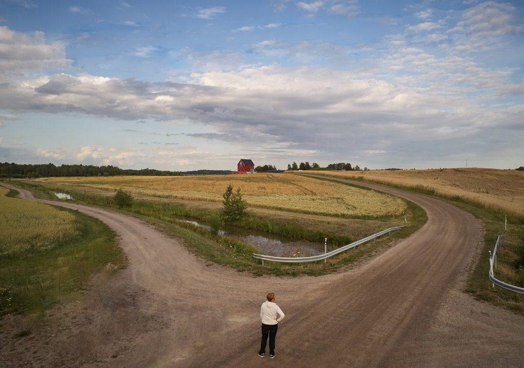 Nainen tienristeyksessä peltojen keskellä