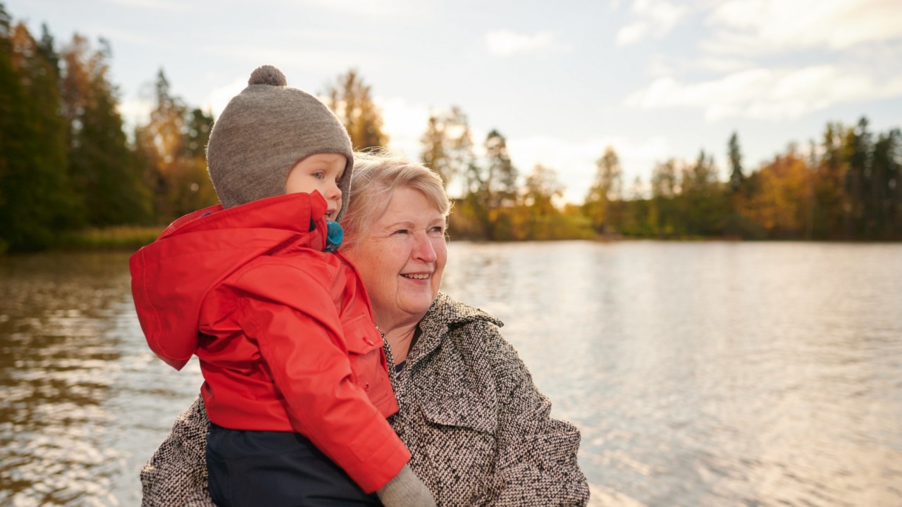 vanha nainen lapsi sylissä järven rannalla.