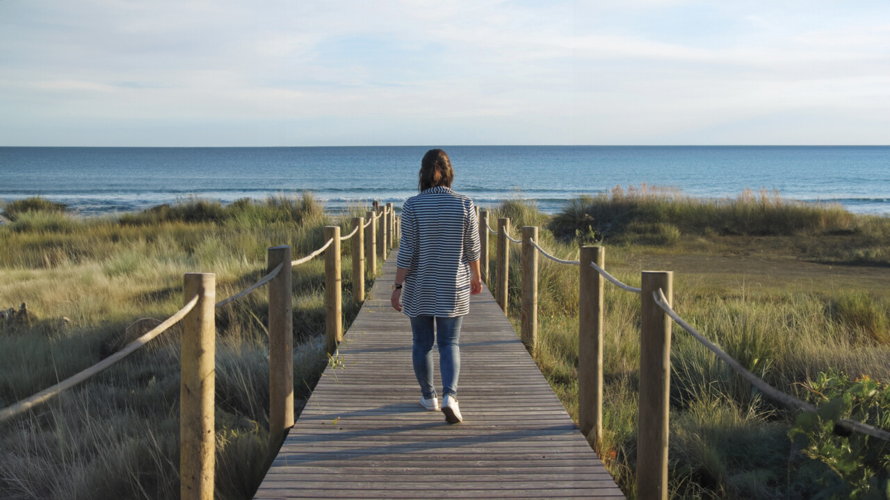 Nainen kävelee laituria pitkin kohti rantaa