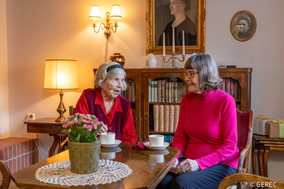 Kaksi ikääntynyttä naista istuvat kahvilla kirjastohuoneessa