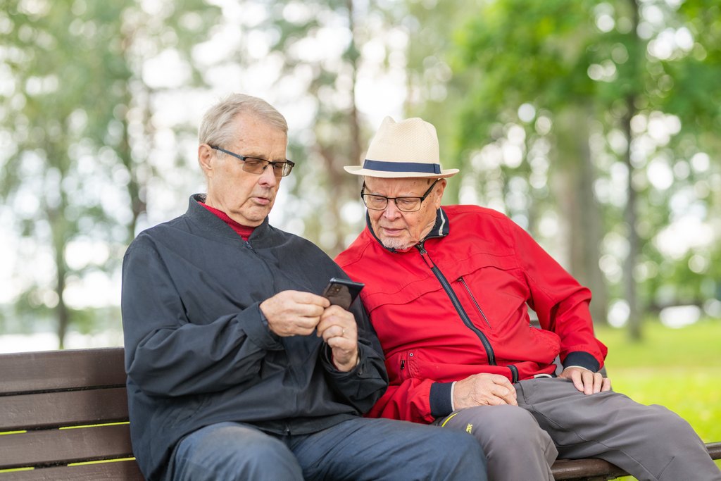 Kaksi miestä katsoo puhelinta puistonpenkillä