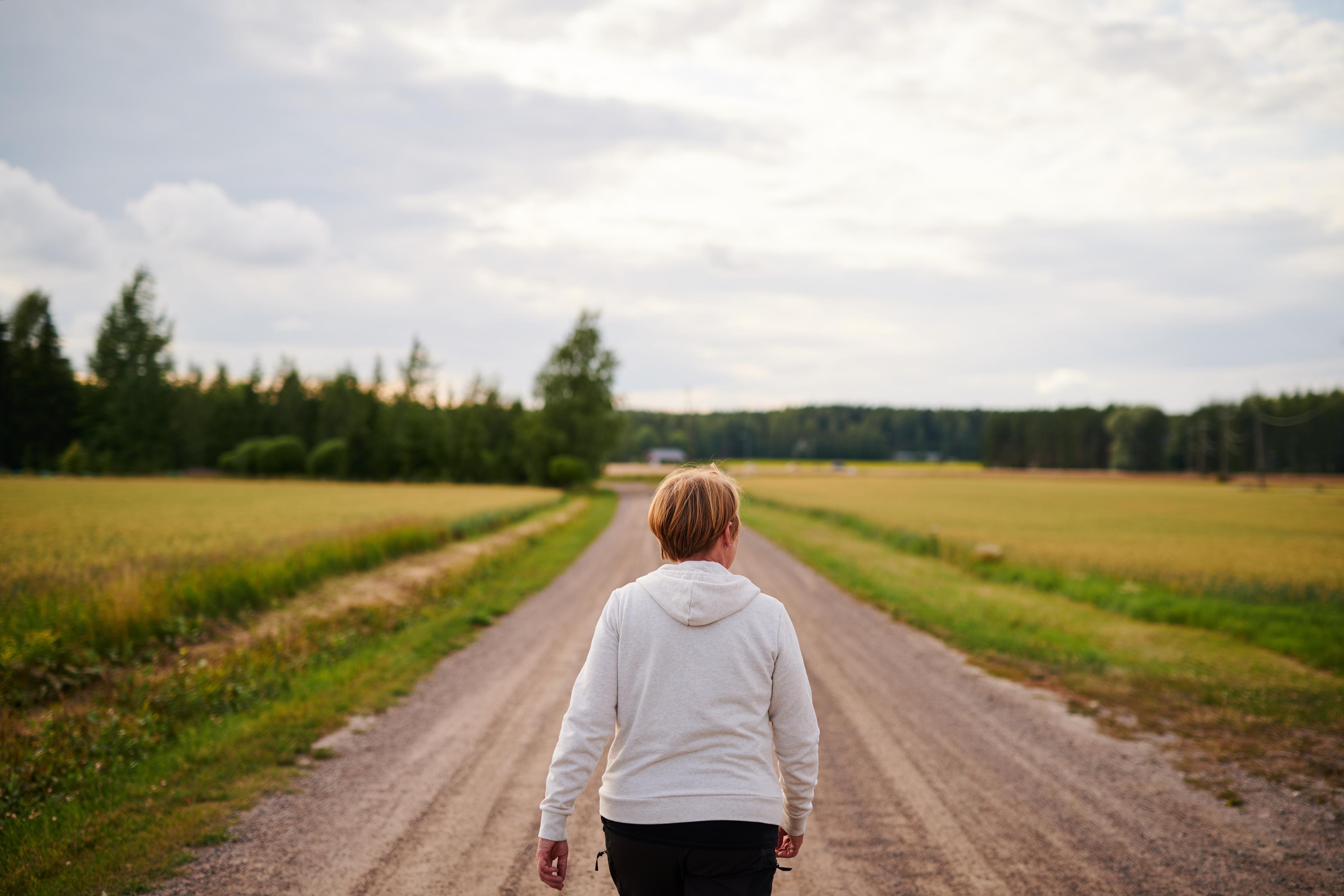Peltomaisemaa, nainen kävelee polkua pitkin.