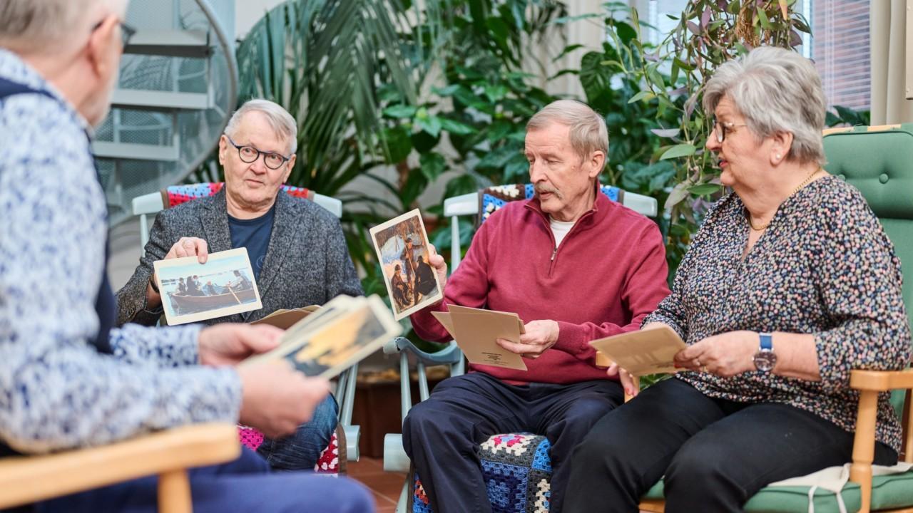 Neljä senioria istuu ja katselee kuvakortteja.